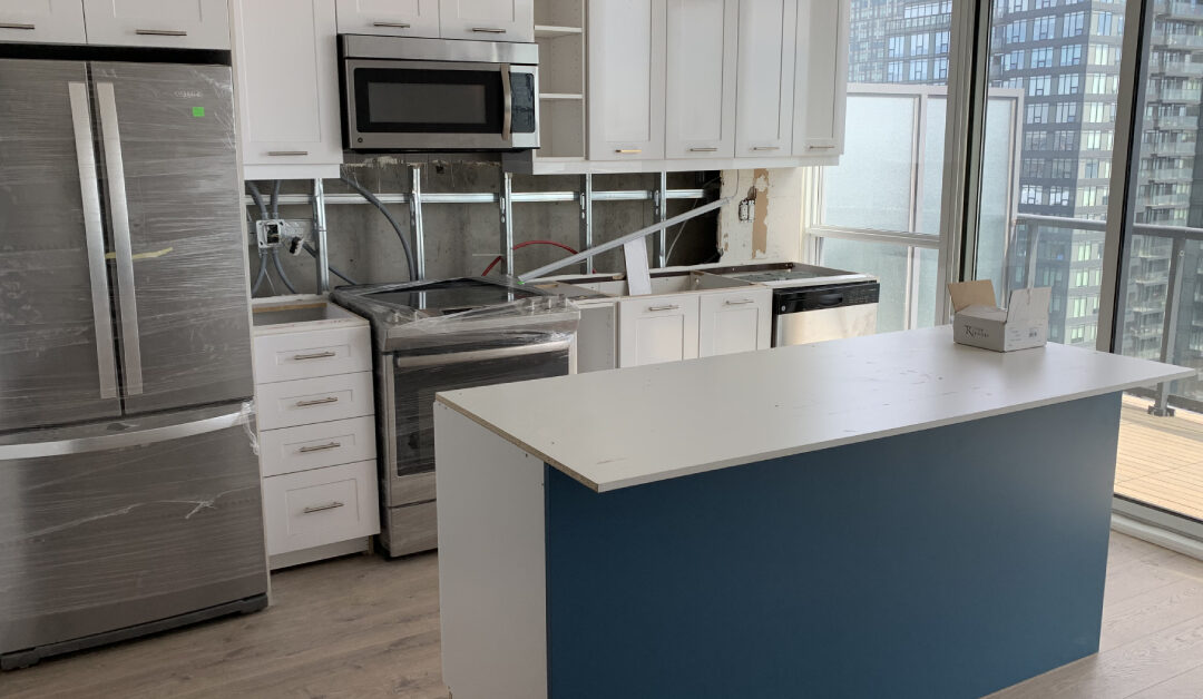 Active condo kitchen renovation in progress by a local kitchen contractor, showing the installation of custom white cabinets, a blue island base, and new stainless steel appliances.