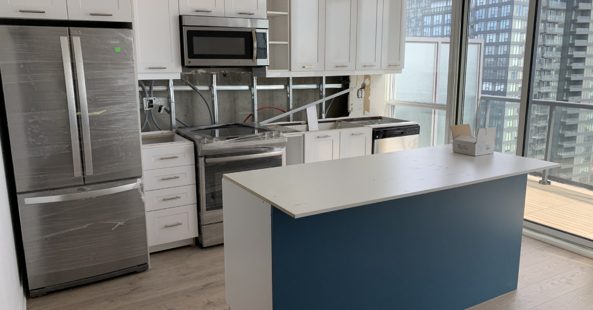 Active condo kitchen renovation in progress by a local kitchen contractor, showing the installation of custom white cabinets, a blue island base, and new stainless steel appliances.