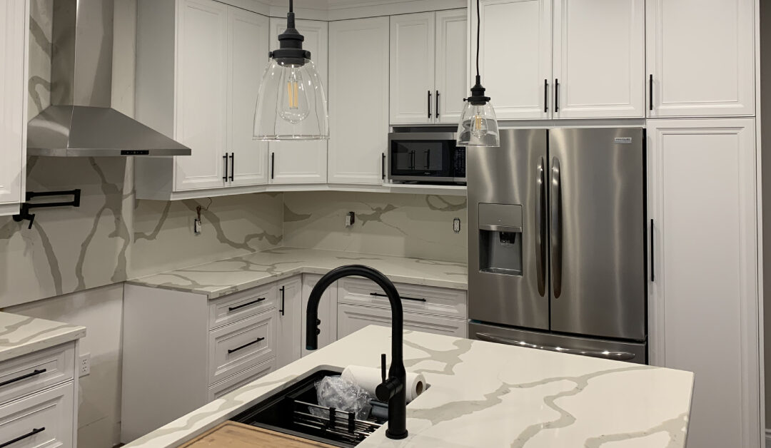 Modern white shaker cabinets and dramatic gray-veined quartz countertops with a full-height matching backsplash in a kitchen renovation project featuring stainless steel appliances.