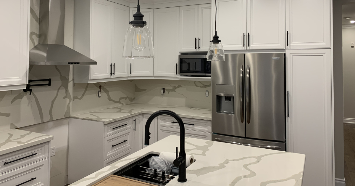 Modern white shaker cabinets and dramatic gray-veined quartz countertops with a full-height matching backsplash in a kitchen renovation project featuring stainless steel appliances.