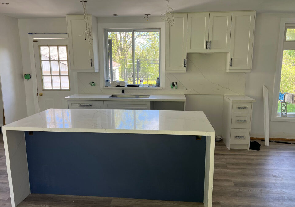 Modern kitchen renovation featuring white shaker cabinets, a blue center island with a white quartz waterfall countertop, full height backsplash, and undermount sink during installation by Envyland Kitchen Cabinet.