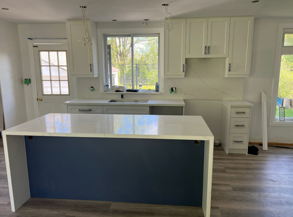 Modern kitchen renovation featuring white shaker cabinets, a blue center island with a white quartz waterfall countertop, full height backsplash, and undermount sink during installation by Envyland Kitchen Cabinet.