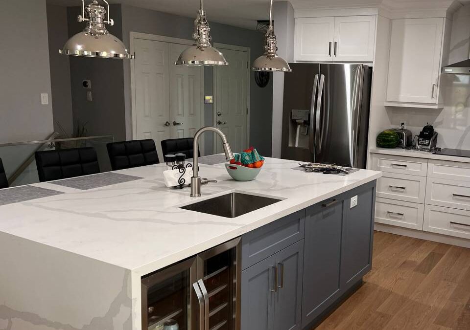Open-concept island kitchen layout with a waterfall white quartz island, slate blue base cabinets, built-in wine fridge, bar seating and white shaker perimeter cabinets in a GTA kitchen renovation by Envyland Kitchen.