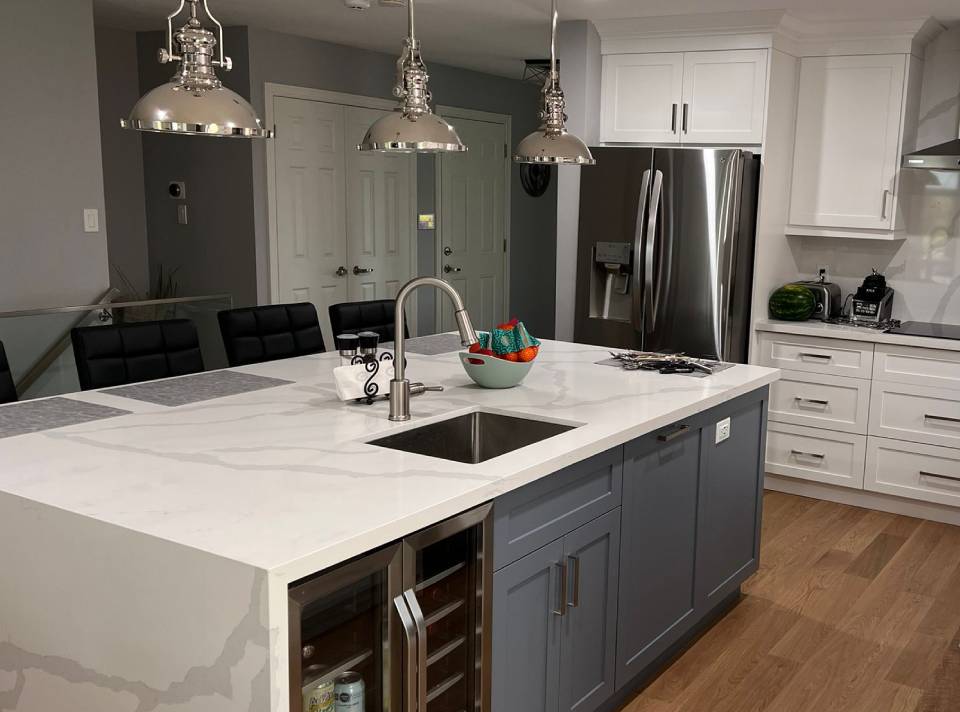 Open-concept island kitchen layout with a waterfall white quartz island, slate blue base cabinets, built-in wine fridge, bar seating and white shaker perimeter cabinets in a GTA kitchen renovation by Envyland Kitchen.